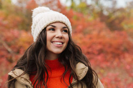 Beautiful brunette happy woman in knit hat smiling while strolling in autumn forest
