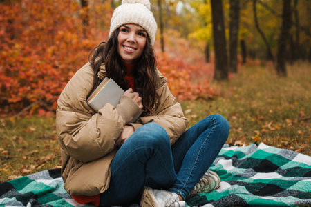 Happy attractive young woman with a book sitting in a autumn park