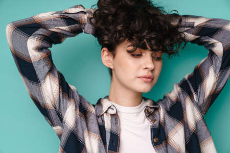 Caucasian beautiful curly girl posing and looking downward isolated over blue backgroundの写真素材