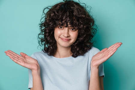 Joyful beautiful curly girl smiling and holding copyspace isolated over blue background