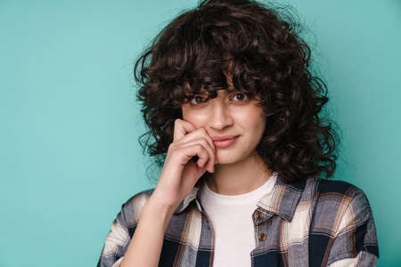 Pleased beautiful curly girl posing and looking at camera isolated over blue background