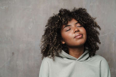 Pleased african american woman posing with eyes closed isolated over grey wallの写真素材