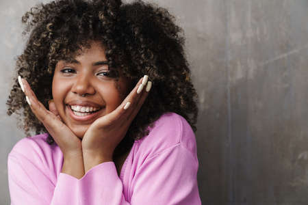Cheerful african american woman posing and smiling at camera isolated over grey wallの写真素材
