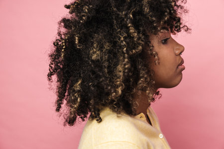 Serious african american woman looking forward while posing in profile isolated over pink wallの写真素材