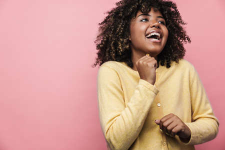 Happy african american woman posing and laughing at camera isolated over pink wall