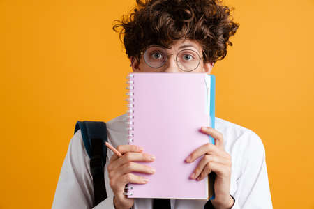 Surprised young male student holding books isolated over yellow background