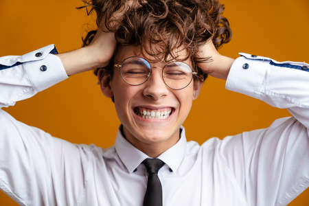 Happy excited male student standing wearing uniform isolated on a yellow backgroundの写真素材