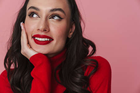 Happy beautiful brunette girl smiling and looking aside isolated over pink backgroundの写真素材