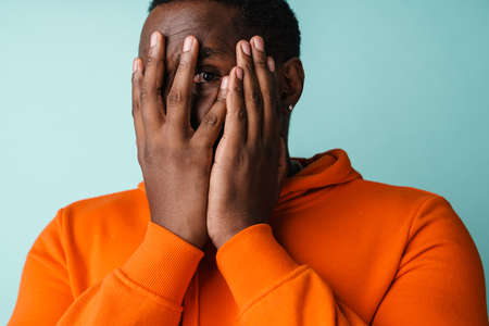Closeup portrait of sad bothered young man completely covering face with hands isolated on blue backgroundの写真素材