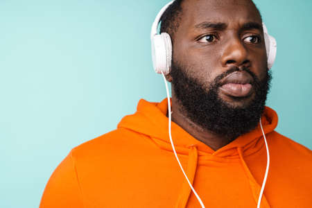 Unshaven african american man listening music with headphones isolated over blue background