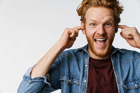 Excited handsome ginger guy exclaiming and plugging his ears isolated over white background