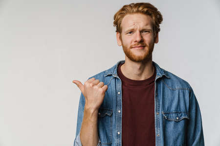 Confused handsome guy posing and pointing finger aside isolated over white backgroundの写真素材