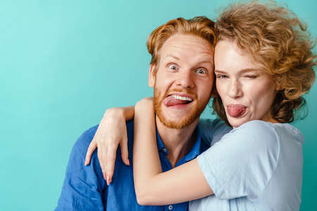 Young cheerful redhead couple hugging and showing her tongues isolated over blue backgroundの写真素材