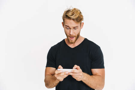 Excited caucasian blonde man playing online game on cellphone isolated over white background