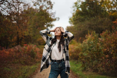 Beautiful brunette happy woman smiling while strolling in autumn forestの写真素材