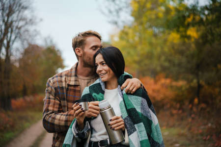 Lovely young couple embracing in the park, covered in blanketの写真素材