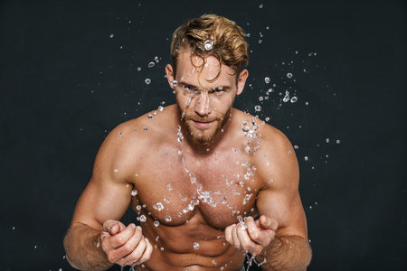 Handsome caucasian shirtless man washing his face isolated over black backgroundの写真素材