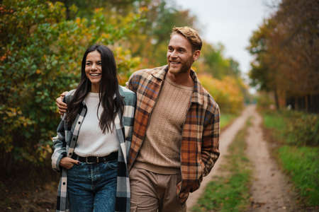 Beautiful happy couple smiling and hugging while strolling in autumn forestの写真素材