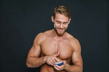 Happy caucasian shirtless man smiling while applying face cream isolated over black backgroundの写真素材