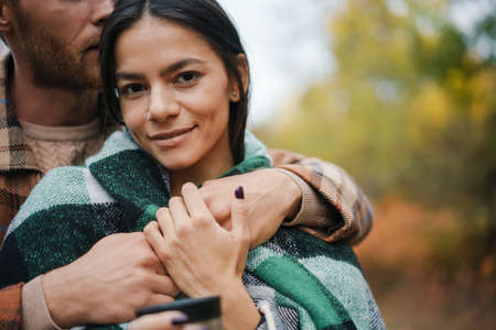 Lovely young couple embracing in the park, covered in blanketの写真素材