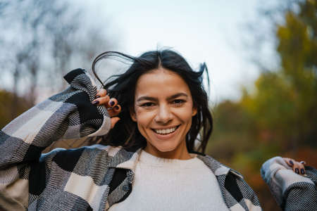 Beautiful brunette happy woman smiling while strolling in autumn forestの写真素材