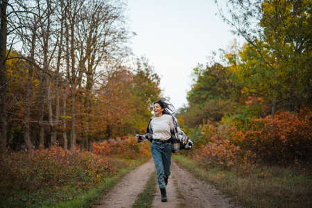 Beautiful brunette happy woman smiling while running in autumn forestの写真素材