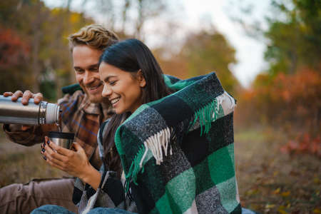 Young happy couple drinking tea and hugging while resting in autumn forest