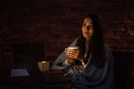 Attractive young asian woman covered in blanket using laptop computer while sitting at the balcony...