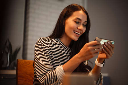 Happy charming woman smiling and using cellphone at home kitchen