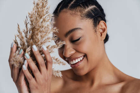 Happy shirtless african american woman posing with dry plant isolated over white backgroundの写真素材