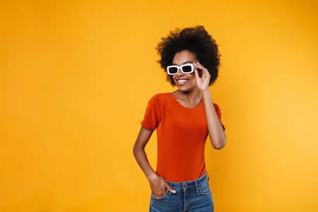 Joyful african american girl in sunglasses smiling and looking aside isolated over yellow backgroundの写真素材