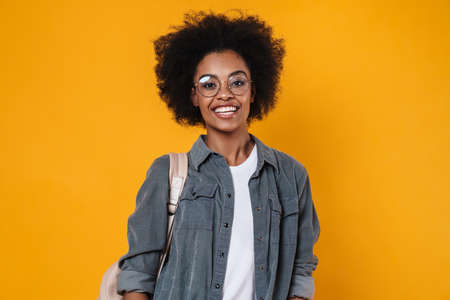 Joyful african american girl in eyeglasses laughing and looking at camera isolated over yellow backgroundの写真素材