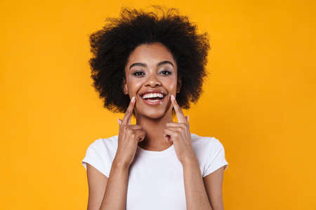 Happy african american girl pointing fingers at her smile isolated over yellow backgroundの写真素材