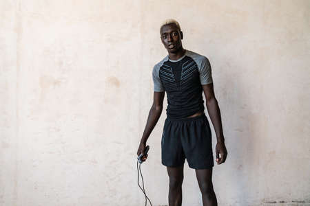 Young athletic african american man holding jumping rope while doing workout indoors