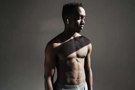 Close up portrait of a handsome fit muscular shirtless sportsman standing isolated over background, using wireless earphonesの写真素材