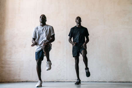 Two young athletic african american men jumping while doing workout indoorsの写真素材