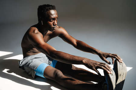 Confident young african sportsman exercising on a fitness mat isolated over gray background,...