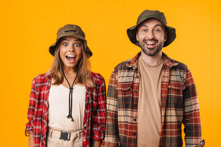 Beautiful excited couple exclaiming and looking at camera isolated over yellow background