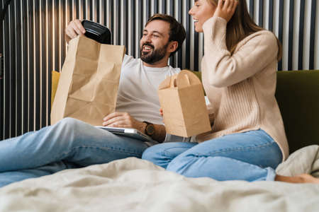 Couple eating take-away food in bedroom, sitting on bedの写真素材