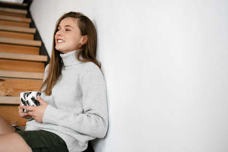 Beautiful smiling nice girl drinking coffee while sitting on staircase at home
