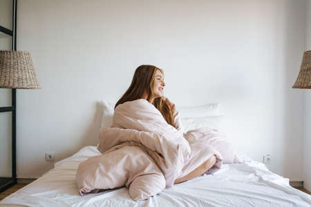 Beautiful cheerful nice girl laughing while sitting on bed at homeの写真素材