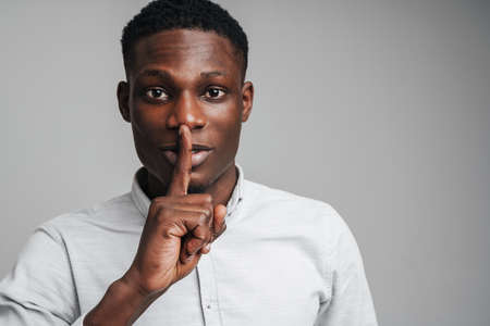 Closeup portrait young businessman placing finger on lips saying, shhh, be quiet, silence, isolated...
