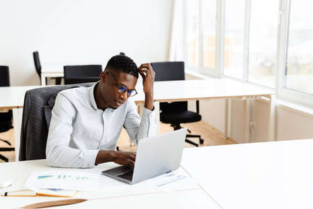 Thoughtful young african american businessman working on laptop computer