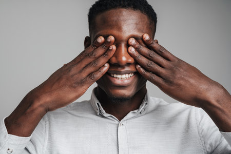 Smiling young african business man covering eyes isolated over gray backgroundの写真素材