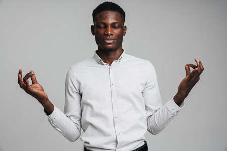 Young businessman meditating, eyes closed, isolated over grey wall background. Stress relief techniques at work conceptの写真素材