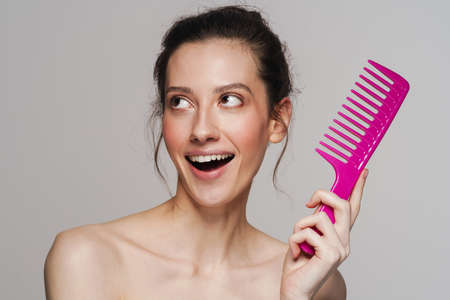 Excited half-naked woman posing with comb on camera isolated over grey backgroundの写真素材
