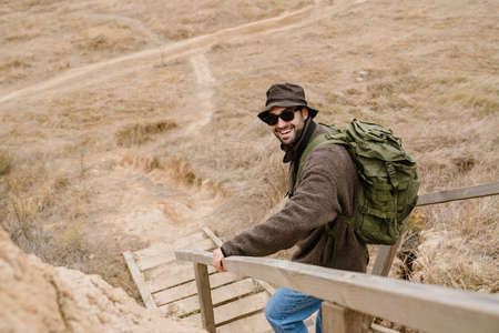 Happy handsome man in sunglasses smiling while going down stairs outdoors