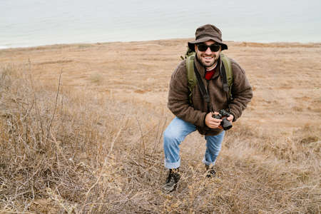 Happy handsome photographer in sunglasses walking with digital camera outdoors