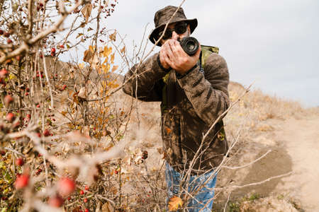 Focused photographer in sunglasses taking photo on digital camera outdoorsの写真素材