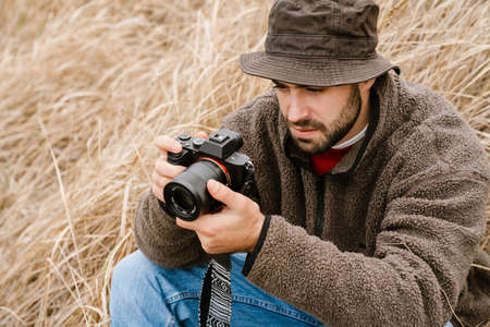Focused handsome photographer taking photo on digital camera outdoorsの写真素材